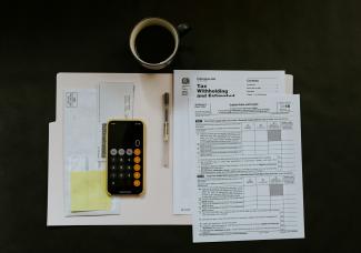 black Android smartphone near ballpoint pen, tax withholding certificate on top of white folder by Kelly Sikkema courtesy of Unsplash.