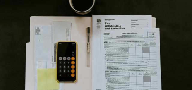 black Android smartphone near ballpoint pen, tax withholding certificate on top of white folder by Kelly Sikkema courtesy of Unsplash.